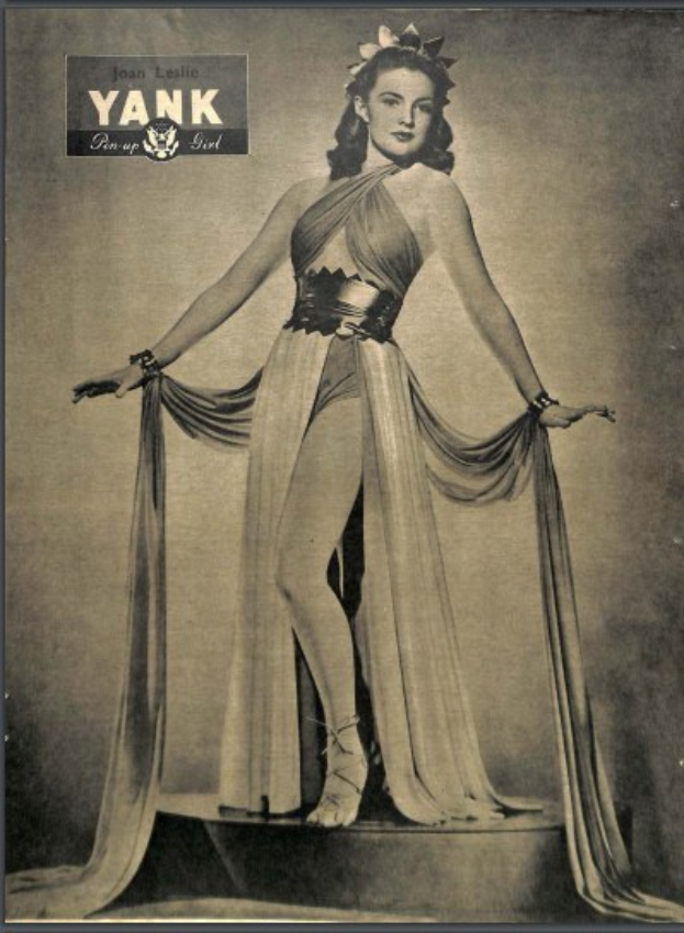 Ein Schwarz-Weiß-Foto der Schauspielerin Joan Leslie, die auf einer Bühne in einem langen, hochgeschlossenen Kleid mit langen Aermeln steht, ihr Haar im Stil der 1940er Jahre frisiert und die Augen geschlossen, eingerahmt von Text, der "Joan Leslie" oben zeigt.