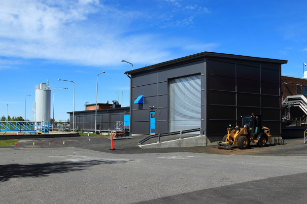 Großes Industriegebäude mit einem Bagger davor, umgeben von Straßeninfrastruktur und Fahrzeugen.