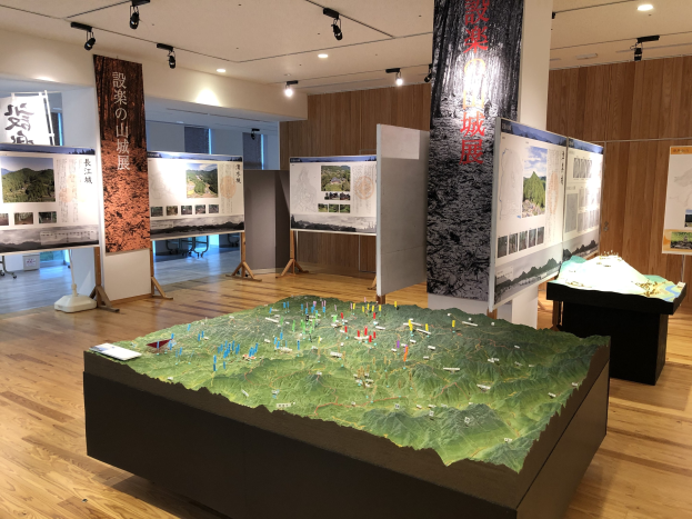 Ausstellungsraum mit verschiedenen historischen Karten Japans, einschließlich montierter Karten, Bannern und Informationsschildern auf Ständern, mit Deckenbeleuchtung und einer hölzernen Rückwand.