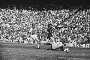 Schwarzes und weißes Foto von Männern, die auf einem Feld Fußball spielen, mit Zuschauern im Hintergrund und einem Banner mit der Aufschrift "Bundesliga 1978-79 Ajax 1:1 Hannover 96."