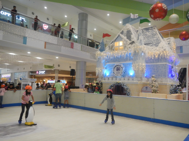 Menschen beim Eislaufen in einer Einkaufszentrum-Rinne umgeben von festlichen Dekorationen, mit Zuschauern und beleuchteten Strukturen.
