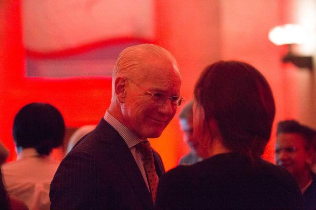 Zwei Menschen in Geschäftsbekleidung in ein Gespräch vertieft, beleuchtet von einem Licht an einer Wand.