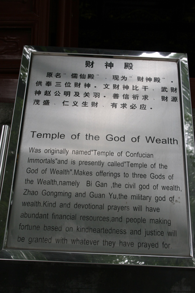 Ein Tempel, der dem Gott des Reichtums gewidmet ist, mit einem Namensschild im Vordergrund und einer T├╝r im Hintergrund, umgeben von üppiger Vegetation.