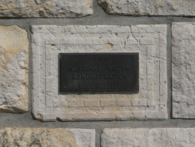 Steinwand mit einem rechteckigen schwarzen Schild, auf dem "National Youth Administration" in weißer, fetter, zentrierter Schrift steht.