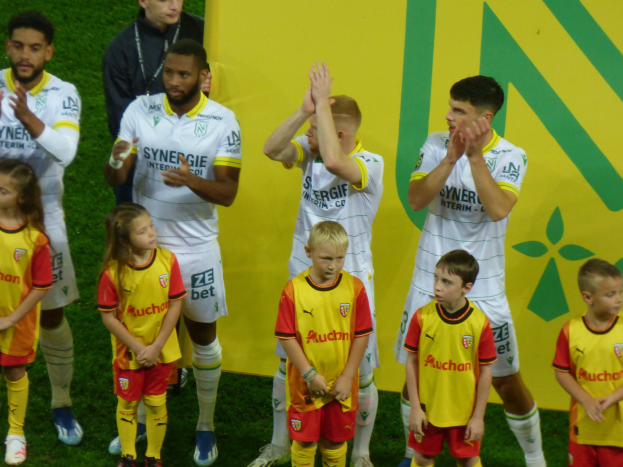 Gruppe von Fußballspielern in Uniformen, die auf einem Feld klatschen, mit einem 'Ligue 1'-Schild im Hintergrund, das einen Sieg feiert.