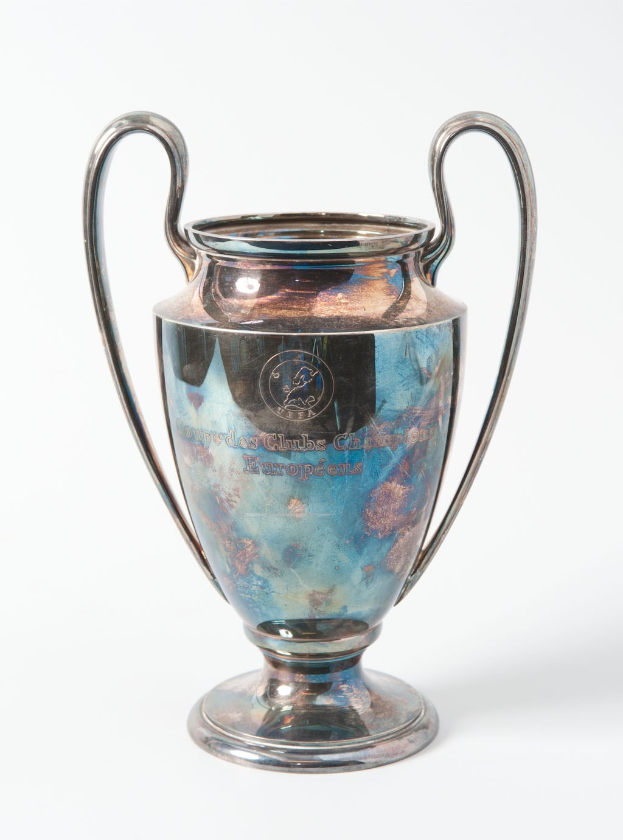 Der UEFA-Champions-League-Pokal, ein stählerner Pokal mit zwei Griffen und einem blauen und silbernen Farbschema, beschriftet mit "UEFA Champions League", vor einem weißen Hintergrund.