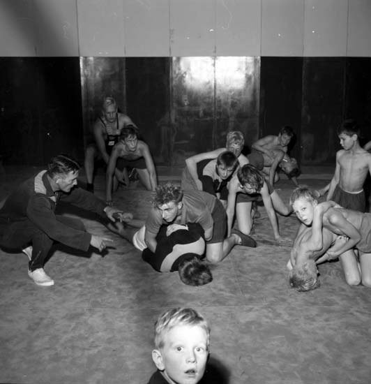 Schwarz-weiß-Foto von jungen Jungs, die in einem Fitnessstudio ringen, mit einer Wand im Hintergrund.