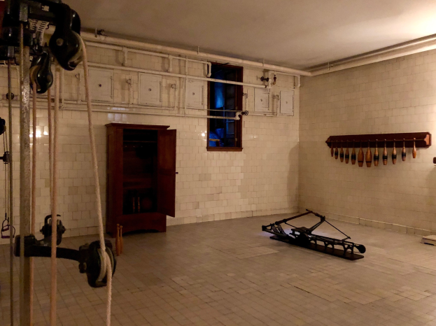 Ein unordentlicher Raum im ehemaligen Gefängnis von St. Louis, Missouri, mit Seilen, Maschinen und anderem Equipment auf dem Boden, einem Schrank im Hintergrund, einer fensterlosen Wand und einer Deckenlampe.