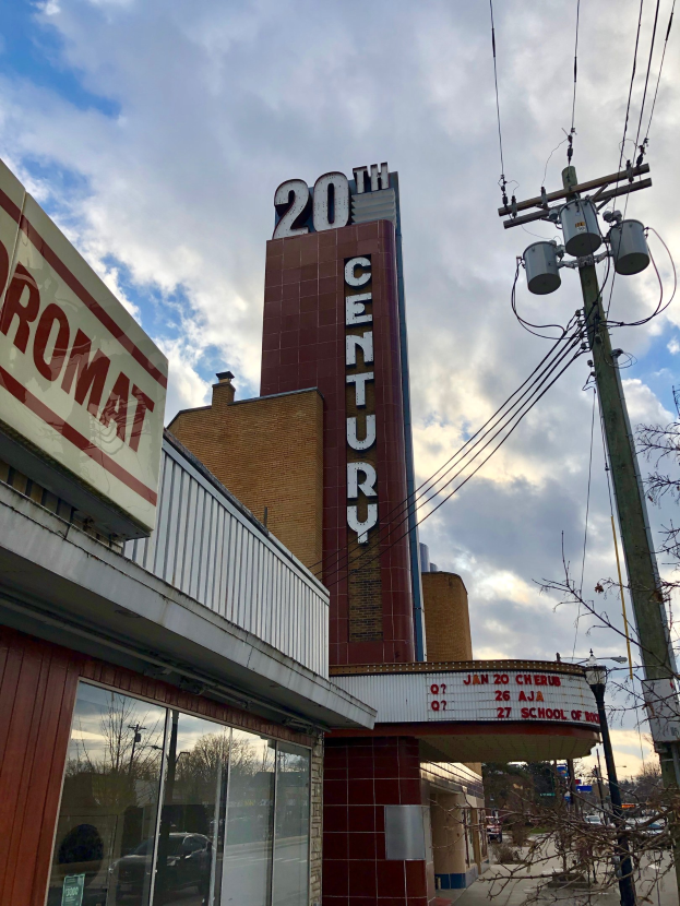 Außensicht des 20. Jahrhundert-Theaters in Detroit, Michigan, mit Glaswänden, Namensschildern, Bäumen, Strommästen mit Drähten und einem bewölkten Himmel.
