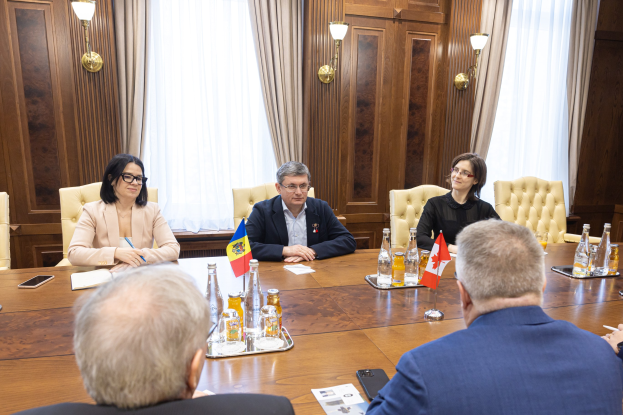 Eine Gruppe von Menschen, die um einen Holztisch in einem formellen Setting sitzen und sich mit EU-bezogenen Materialien auf dem Tisch beschäftigen.