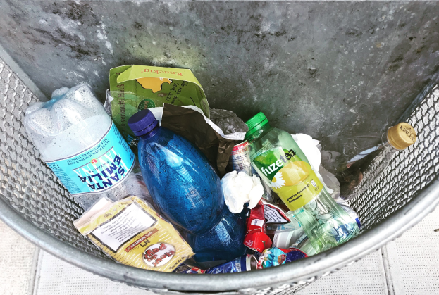 Metallmülltonne mit verschiedenen Plastikflaschen, Tüten und anderen Gegenständen.