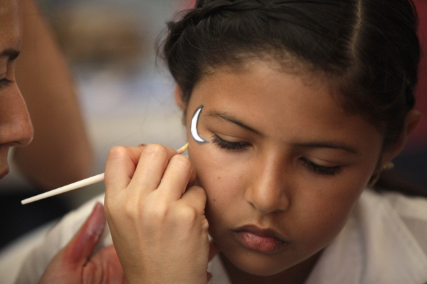Ein Make-up-Künstler trägt Make-up auf das Gesicht eines jungen Mädchens auf, während der Hintergrund unscharf ist.