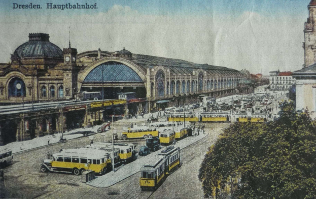 Schwarz-weiß-Postkarte vom Dresdner Hauptbahnhof mit einer belebten Straße, Autos, Fußgängern, Bäumen, Gebäuden und einem bewölkten Himmel.