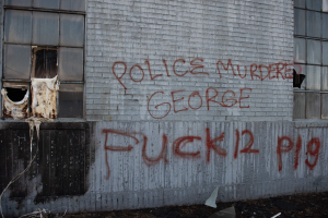 Ein Gebäude mit Graffiti, das "Polizei ermordet George Fuck 12 P19" lautet, mit Fenstern und verschiedenen Gegenständen davor.