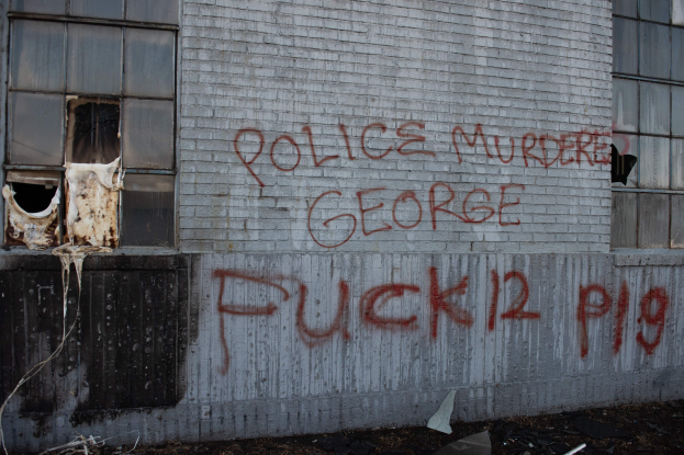 Ein Gebäude mit Graffiti, das "Polizei ermordet George Fuck 12 P19" lautet, mit Fenstern und verschiedenen Gegenständen davor.