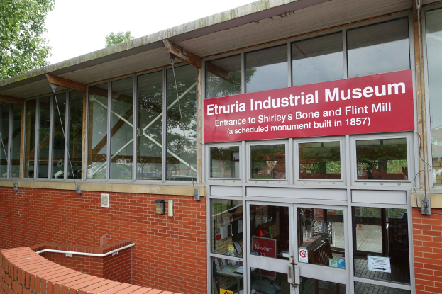 Außenansicht des Etruria-Industrie-Museums mit Glaswänden, einem Textschild, einer Backsteinwand, einem Geländer, Bäumen und einem klaren blauen Himmel.