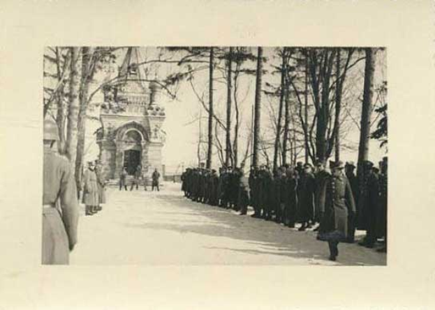 Schwarzes und weißes Foto einer Gruppe von Menschen, die vor einem Gebäude mit einem Bogen im Hintergrund und Bäumen an der Straße stehen, mit Text unten, der "Die Beerdigung der Opfer der Berliner Mauer" lautet.