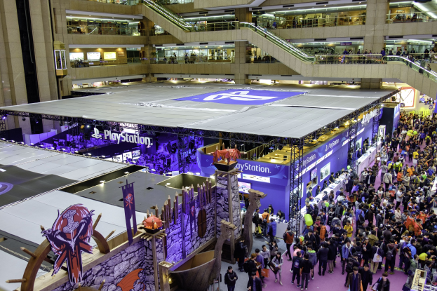 Eine große Menschenmenge in einem geräumigen Konferenzzentrum mit Rolltreppen, Geländern, beleuchteten Schildern, Bannern und anderen Anzeigen, die die größte Gaming-Messe der Welt anzeigen.