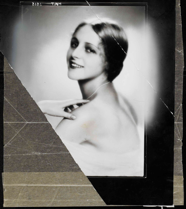 Schwarz-weißes Porträt einer Frau in einem Kleid im Stil der 1920er Jahre mit ihrem Haar zu einem ordentlichen Knoten frisiert, die warm in die Kamera lächelt.