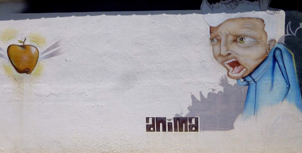 Eine Wandmalerei auf der Seite eines Gebäudes zeigt einen Mann in einem blauen Hemd mit einem verschmitzten Ausdruck, der einen leuchtend gelben Apfel auf seinem Kopf hölt, mit der Aufschrift "Puma" an der Wand.