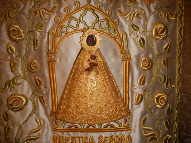 Goldene Stickerei mit einem Bild einer Frau in einem langen, hochgeschlossenen Kleid mit einem Knoten, umgeben von detaillierten Designs und prunkvollen Texten in einem goldenen Rahmen.