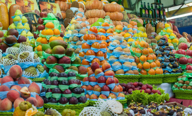 Ein Marktstand mit Äpfeln, Orangen, Birnen und anderen Früchten und Gemüsen, mit Flaschen auf Regalen und Deckenbeleuchtung.