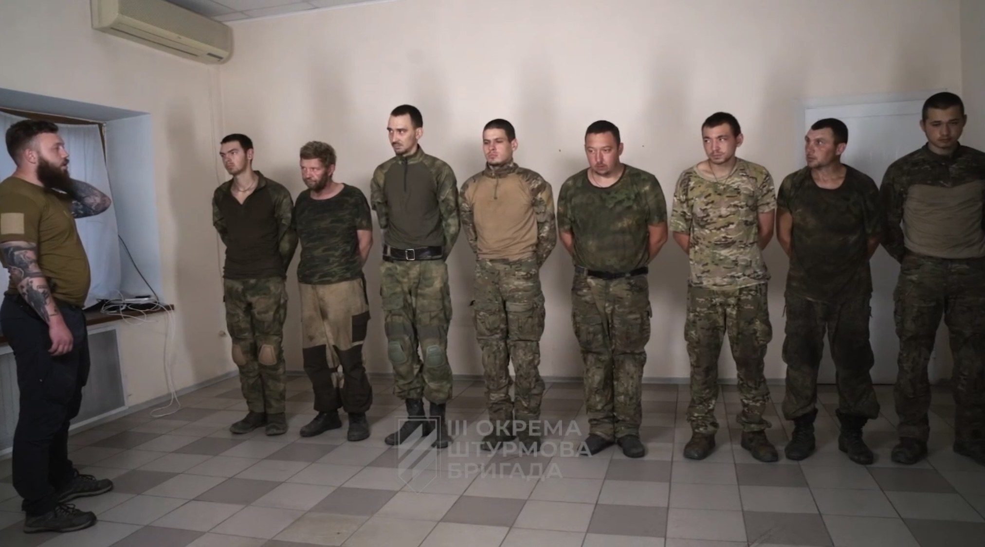 Gruppe von Männern in militärischer Uniform, die in einem Raum mit einer wandmontierten Klimaanlage, einer Tür auf der rechten Seite und einem Tisch mit Gegenständen stehen; Text unten lautet "Sergei Vorobyov und sein Team."