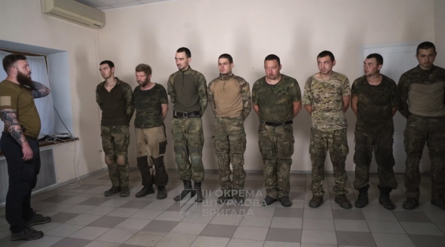 Gruppe von Männern in militärischer Uniform, die in einem Raum mit einer wandmontierten Klimaanlage, einer Tür auf der rechten Seite und einem Tisch mit Gegenständen stehen; Text unten lautet "Sergei Vorobyov und sein Team."