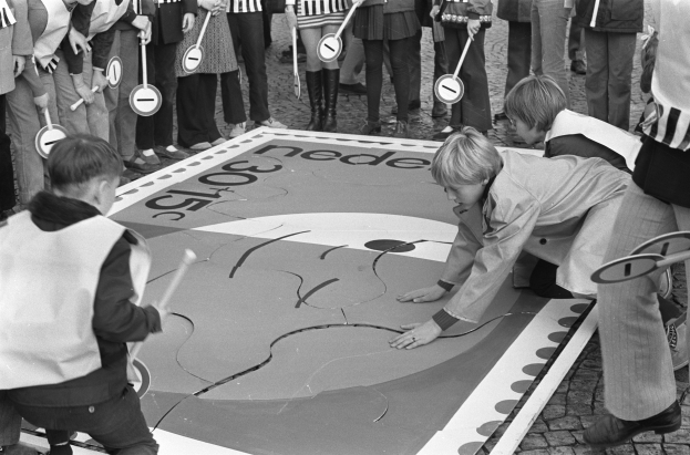 Schwarz-weißes Foto von Kindern beim Hüpfen, einige halten Stöcke.
