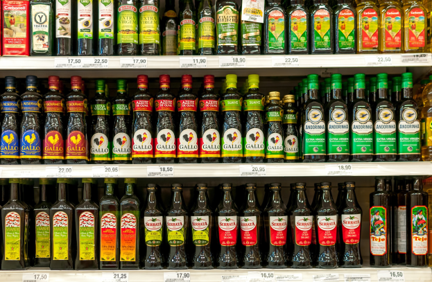 Ein Regal mit verschiedenen Olivenölflaschen in unterschiedlichen Etiketten und Preisschildern, ordentlich angeordnet.