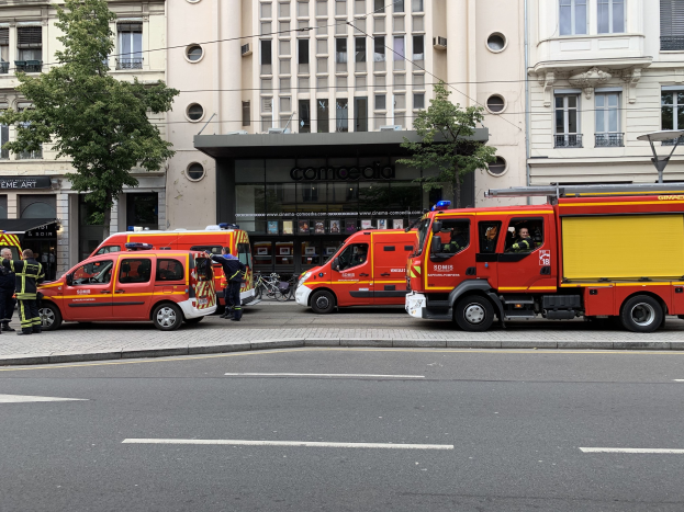 Gruppe von Feuerwehrautos auf einer Straße in Paris geparkt mit Menschen in der Nähe, Gebäuden, Bäumen und einem Fahrrad im Hintergrund, wahrscheinlich nach einem Unfall.