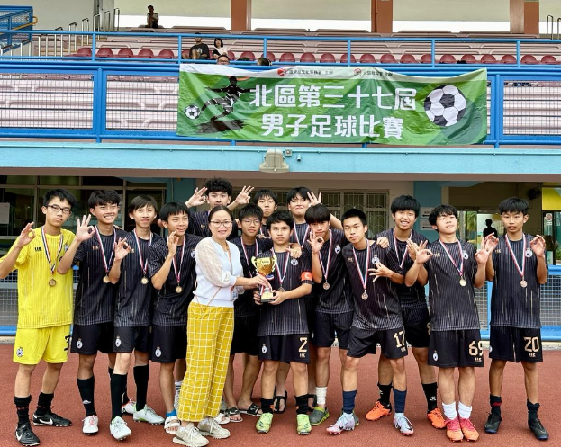 Gruppe junger Männer in Fußballtrikots auf einem Feld mit einem Pokal und Medaillen, im Hintergrund eine Wand mit der Aufschrift "Yokohama U-16 Jungenfußballmannschaft".