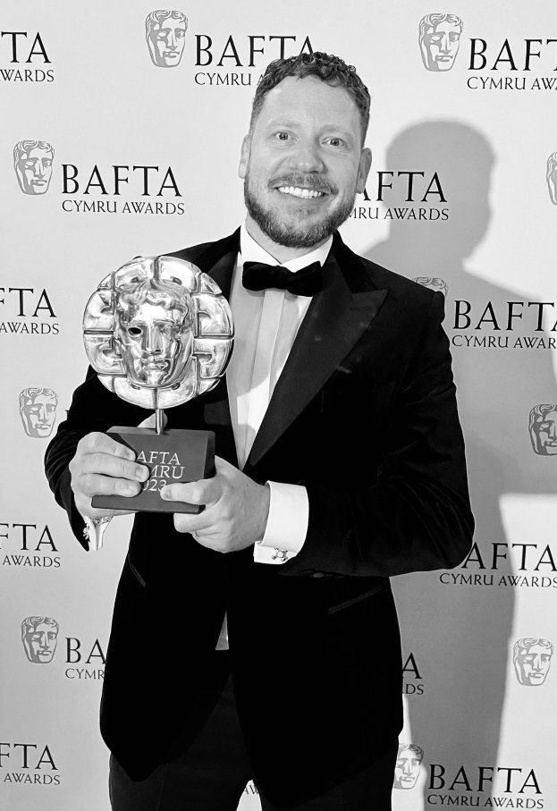 Ein Mann im Smoking lächelt, während er einen BAFTA-Award hält, mit einem 'BAFTA Awards 2018'-Schild im Hintergrund.