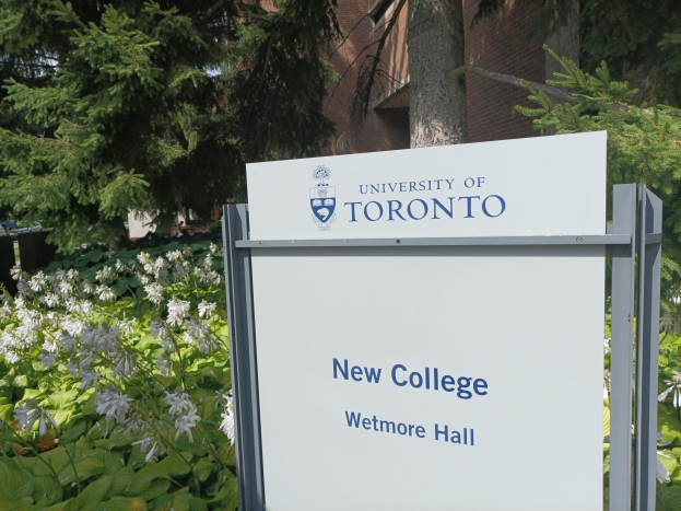 Außenansicht des neuen Colleges der Universität Toronto an Wetmore Hall mit einem Schild davor, umgeben von grünem Gras, bunten Blumen, hohen Bäumen und einem klaren blauen Himmel.