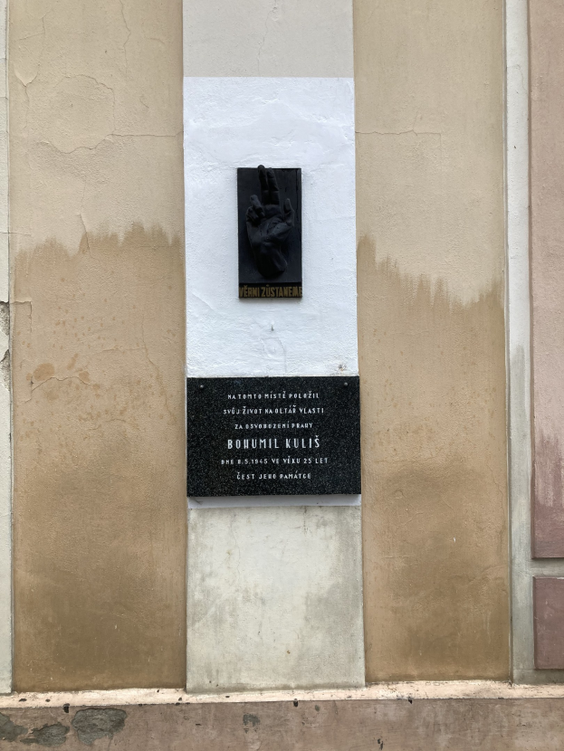 Schwarze Tafel an einem Gebäude mit einer darauf ruhenden Hand, die mit Text beschriftet ist, der Holocaust-Opfer gedenkt.