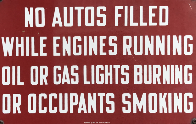 Ein rotes Schild mit weißer Schrift, das davor warnt, Autos aufzufüllen, während die Motoren laufen, Öl- oder Gaslampen brennen oder Insassen rauchen.