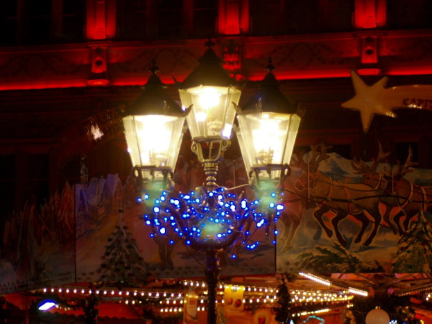Eine festlich geschmückte Straßenlaterne in der Nacht in einer Stadt, mit einem Gebäude im Hintergrund.