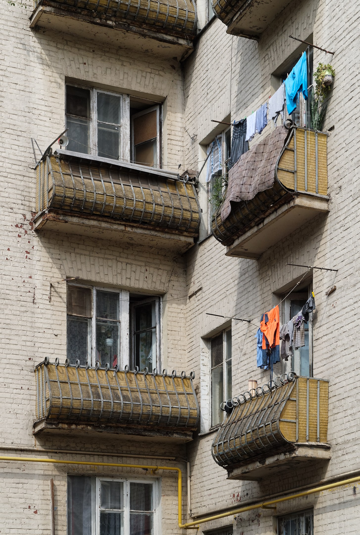 Wohngebäude mit Fenstern, Balkonen, Wäsche zum Trocknen und Außenschläuchen.