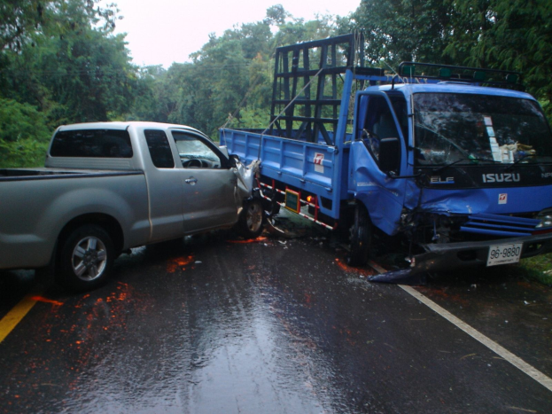 Ein geschädigter Lkw mit eingedellter Front und verbeulter Karosserie auf der Seite einer Straße, umgeben von Bäumen unter einem klaren blauen Himmel.