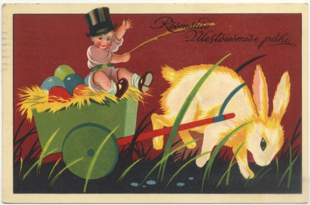 Alte Postkarte mit einem Baby in einem Zylinder, das einen mit bunten Ostereiern gefüllten Schubkarren schiebt, begleitet von einem Kaninchen, mit handgeschriebenen Ostergrü├čen.
