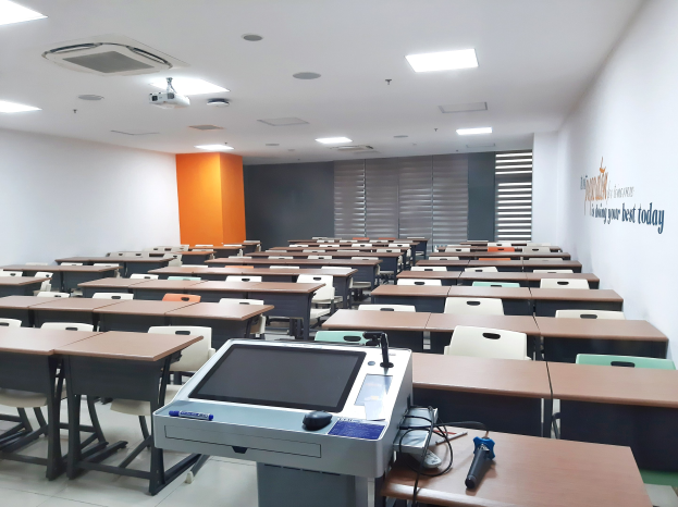 Klassenzimmer mit Tischen und Stühlen in Reihen, Deckenprojizierer, Tische mit Gegenständen und Text an der Wand, der eine Privatschule in Singapur angibt.
