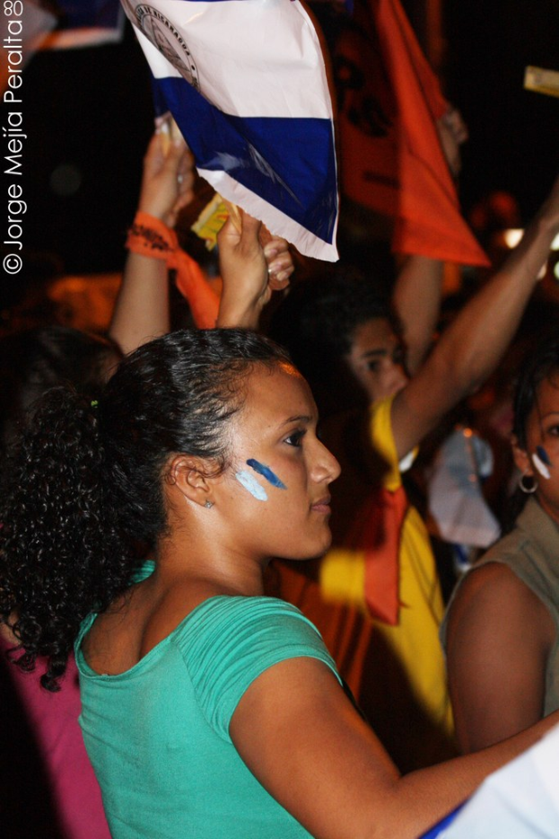 Frauen in grünen T-Shirts bei einer Demonstration mit weißen Decken, mit mehreren Mädchen im Hintergrund.