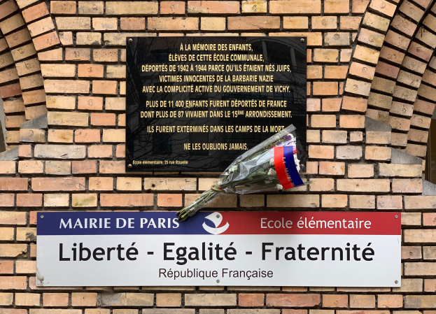 Eine Ziegelwand mit einem Schild, auf dem "Liberté - Egalité - Fraternité" steht und ein Blumenstrauß davor, wahrscheinlich ein Denkmal in Paris, Frankreich.