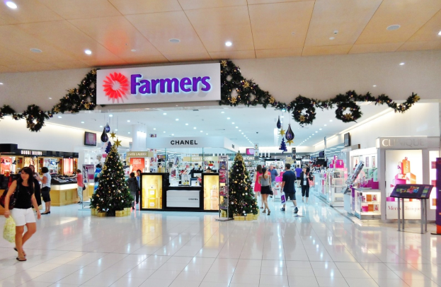 Menschen gehen durch ein Weihnachtsdekorationen Einkaufszentrum mit beleuchteten Bäumen, festlichen Dekorationen und einer Deckenanzeigetafel, einige mit Einkaufstaschen.