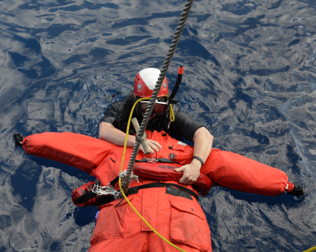 Ein Retter in roter Schwimmweste und Helm treibt im Wasser mit einem Seil auf dem Rücken.