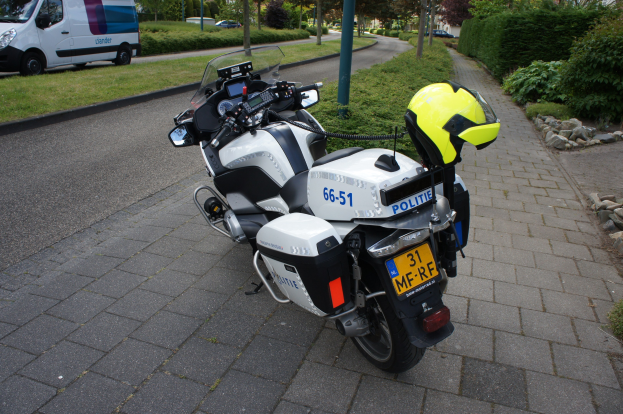 Ein auf der Seite der Straße geparktes Polizeimotorrad mit einem Helm darauf, umgeben von Bäumen, Gebäuden und anderen Fahrzeugen.