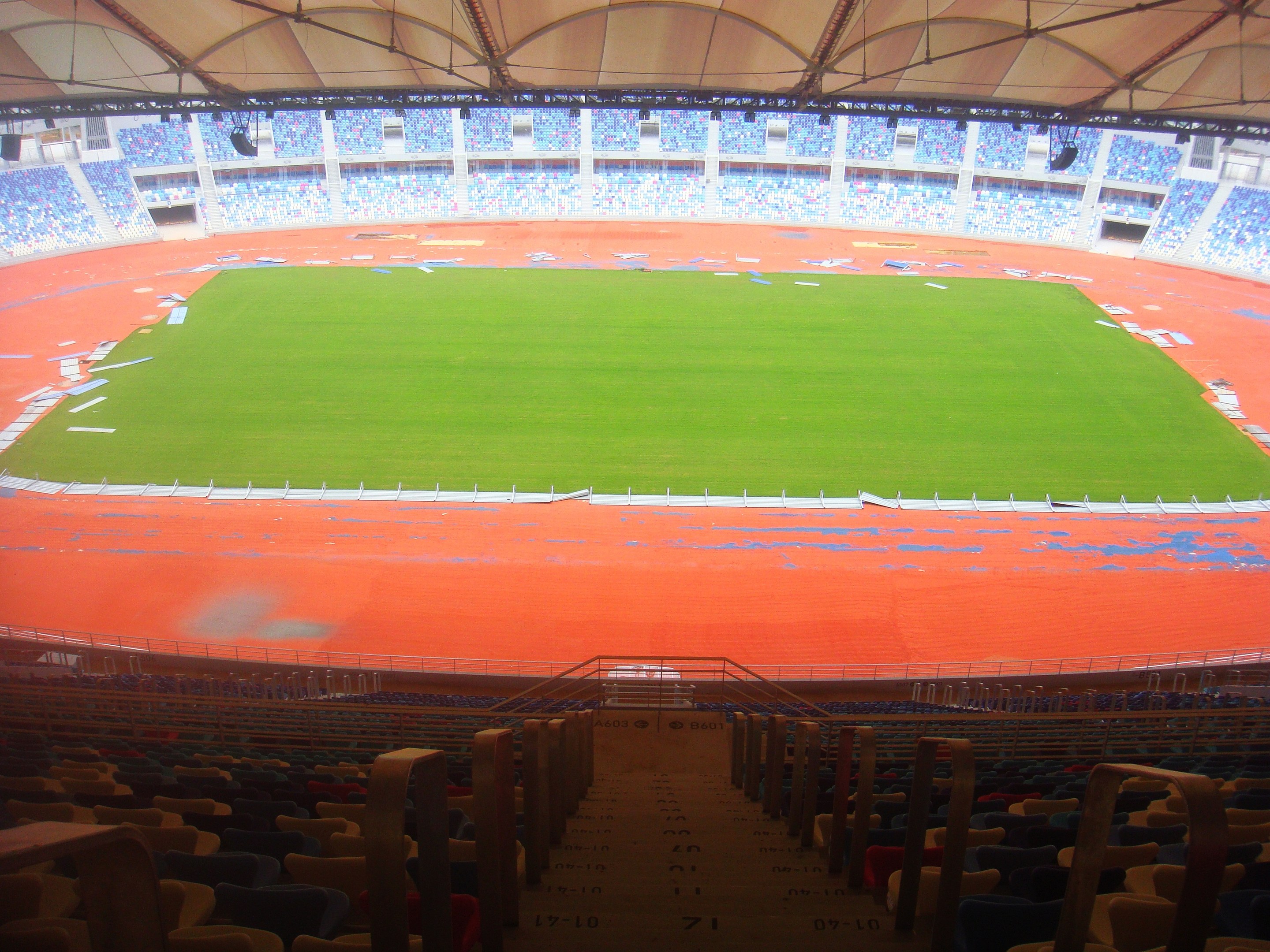 Ein großes Stadion voller Zuschauer mit Sitzreihen, Geländern, Treppen und einem Dach, mit dem Spielfeld in der Mitte sichtbar.