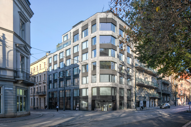 Großes modernes Bürogebäude mit zahlreichen Fenstern, umgeben von Straßeninfrastruktur einschließlich Masten, Lampen und Kabeln, mit Fahrzeugen, Fußgängern, Bäumen und einem bewölkten Himmel im Hintergrund.