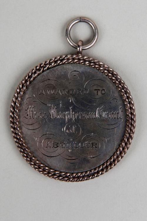 Silberne Medaille mit schwarzem Text "Ausgezeichnet an den Metropolitan Council" auf einem dekorativen Rand, an einem Seil hängend.