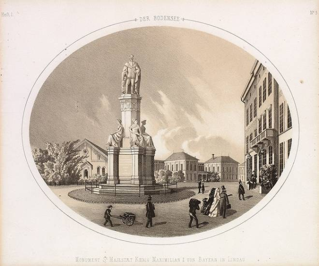 Schwarz-weiß-Zeichnung einer Statue des Heiligen Majestrat König Maximilian I. von Bayern in einem Stadtplatz, umgeben von Gebäuden, Bäumen und Menschen, mit Text unten.